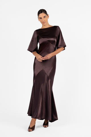 One Fell Swoop Moni Gown in Aubergine, crafted from lustrous plum satin. Designed with a graceful bateau neckline, sculptural bias panelling, and elegant elbow-length sleeves for a timeless silhouette.