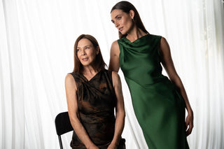 Model wearing emerald green satin maxi dress with draped cowl neckline beside dark abstract print sleeveless midi dress against soft white backdrop.