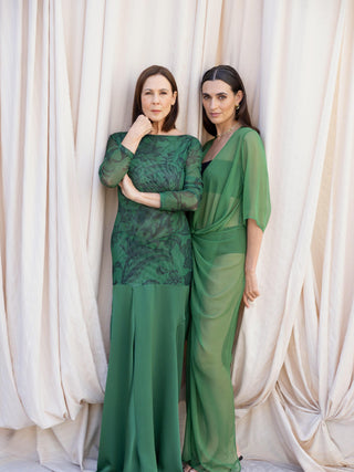 Emerald green sheer mesh maxi dress with tonal floral print beside draped sheer green wrap dress against soft neutral backdrop.