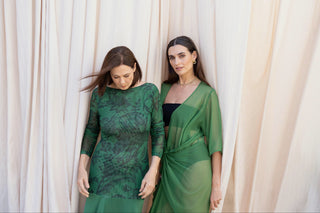 Emerald green sheer mesh maxi dress with tonal floral print beside draped sheer green wrap dress against soft neutral backdrop.