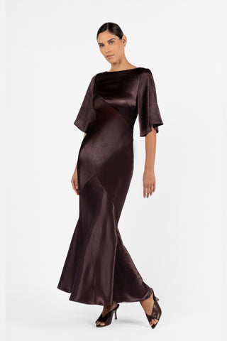 One Fell Swoop Moni Gown in Aubergine, crafted from lustrous plum satin. Designed with a graceful bateau neckline, sculptural bias panelling that showcases movement.