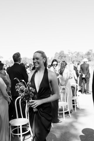 Black and white photograph of bridesmaid wearing the One Fell Swoop Talia Dress in Obsidian at an outdoor wedding ceremony