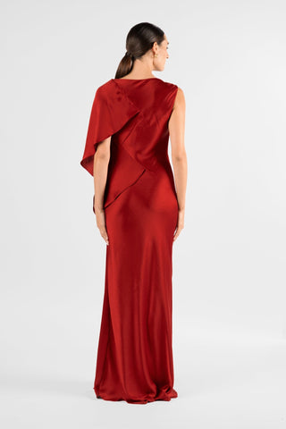 One Fell Swoop Glinch Gown in Carmine, back view of the deep red satin gown: a round, high back neckline with a draped panel sweeping over one shoulder like a short cape, then a smooth fitted back falling into a flared, floor-length bias-cut skirt.