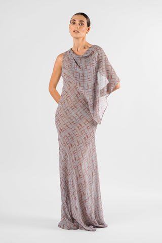 One Fell Swoop Glinch Gown in Ink Veil, front view with both hands behind the hips, showing the cape-like chiffon panel falling from one shoulder and sheer, softly draped over the arm, the cowl neckline and the fitted bodice flowing into a long printed skirt.