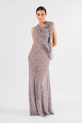 One Fell Swoop Glinch Gown in Ink Veil, front three-quarter view with one hand at the hip, showing the cowl neckline, the narrow chiffon drape falling from the shoulder down one side of the bodice and the sheer grey and rust-red printed skirt flowing to the floor.