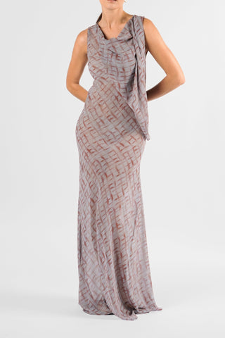 One Fell Swoop Glinch Gown in Ink Veil, close three-quarter view with hands behind the hips, showing the cowl neckline, the vertical chiffon drape at the shoulder, the sleeveless bodice and the fitted waist and hips of the sheer grey and rust-red printed gown.