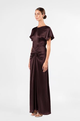 One Fell Swoop Kiera Dress in Aubergine, side three-quarter view showing the flutter sleeve, the bateau neckline, the ruched gathering at the waist and hip and the fluid, flared satin skirt.